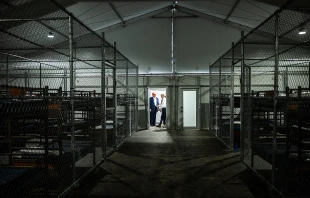 Rows of bunk beds line the interior of the so-called “Alligator Alcatraz” detention facility in the Florida Everglades, a repurposed training center now designated for holding immigrants. President Donald Trump appears in the background during a July 1, 2025, visit to the site. Credit: The White House, Public domain, via Wikimedia Commons
