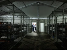 Rows of bunk beds line the interior of the so-called “Alligator Alcatraz” detention facility in the Florida Everglades, a repurposed training center now designated for holding immigrants. President Donald Trump appears in the background during a July 1, 2025, visit to the site.